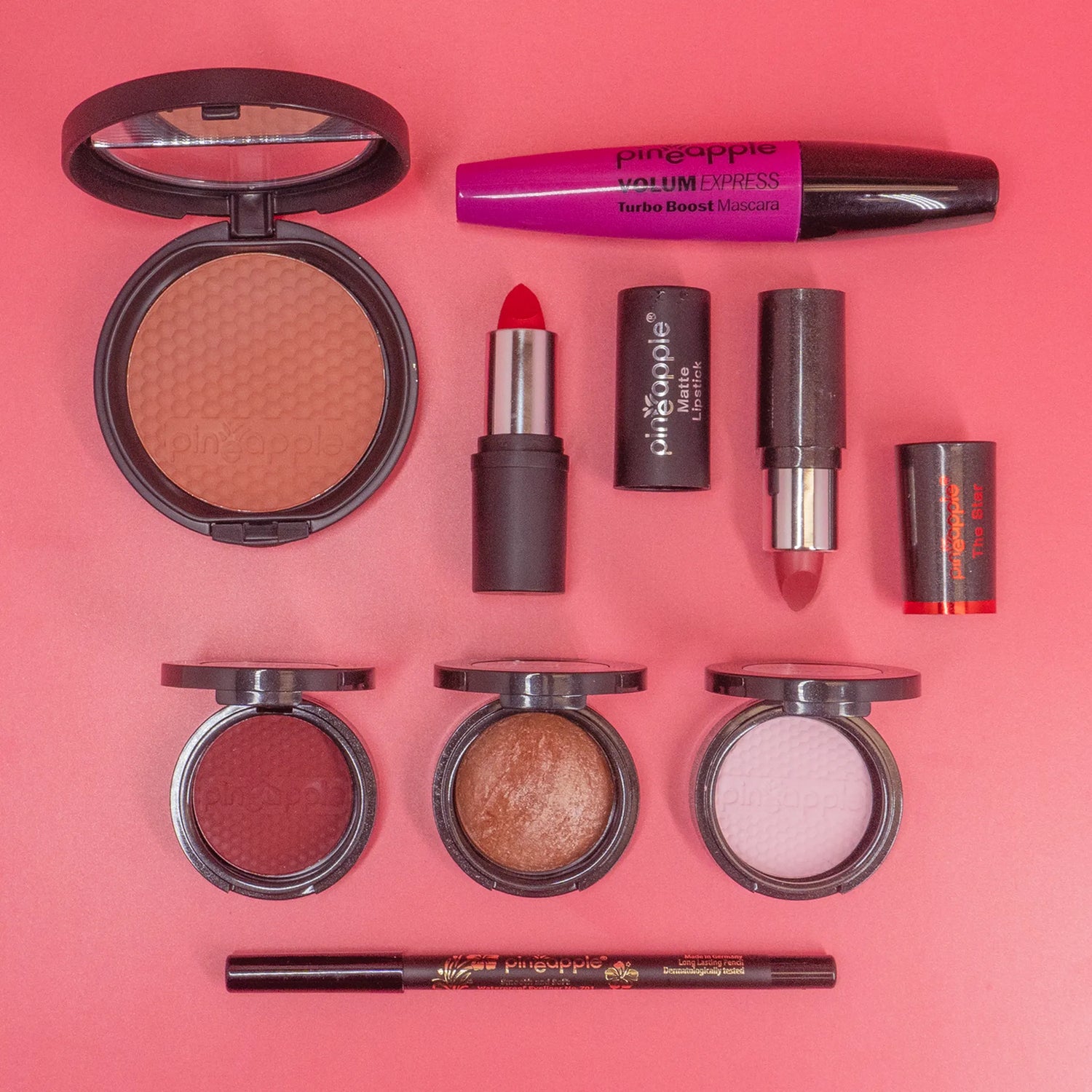 Collection of makeup products including blush, lipstick, and mascara on a pink background